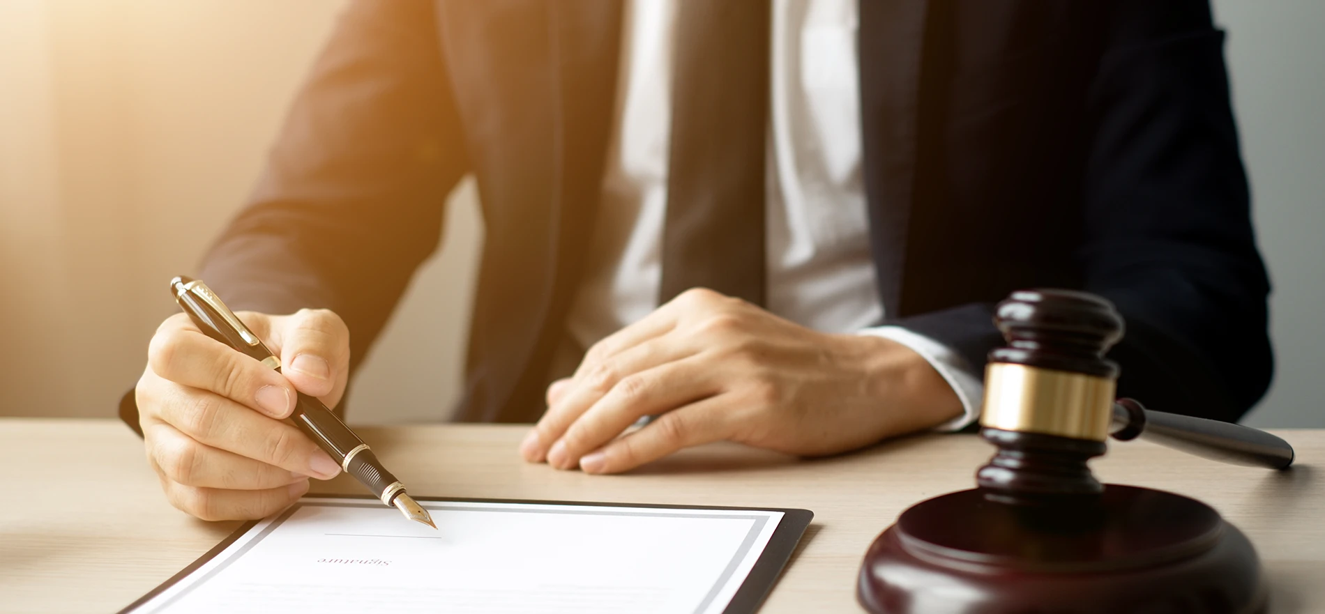 Attorney holding a pen over a legal document with a wooden judge's gavel on the desk